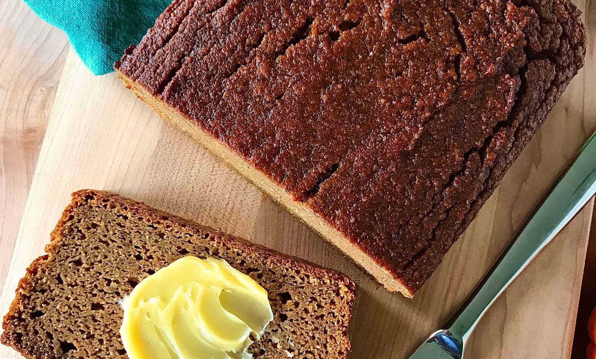 a paleo pumpkin bread loaf with a slice smeared with butter on a cutting board