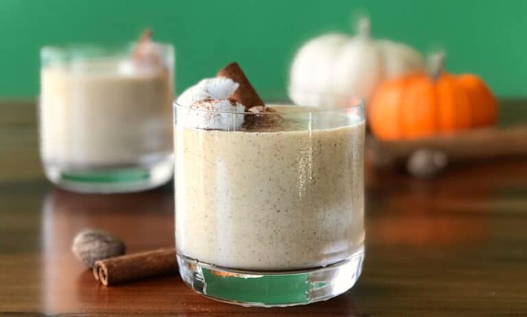 a healthy pumpkin smoothie in a glass topped with whipped coconut cream and a cinnamon stick