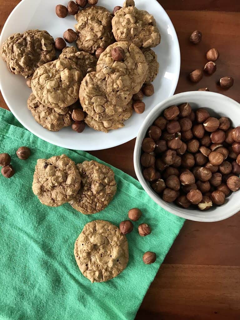 Italian hazelnut cookies on a white plate and a green napkin next to a bowl of hazelnuts