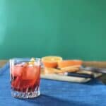 a classic Campari cocktail with vermouth and Prosecco in a glass with ice and an orange slice next to a cutting board with oranges on it