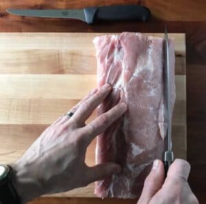 two hands using a knife to slice down a boneless pork loin