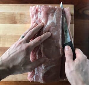two hands using a boning knife to slice into a pork loin