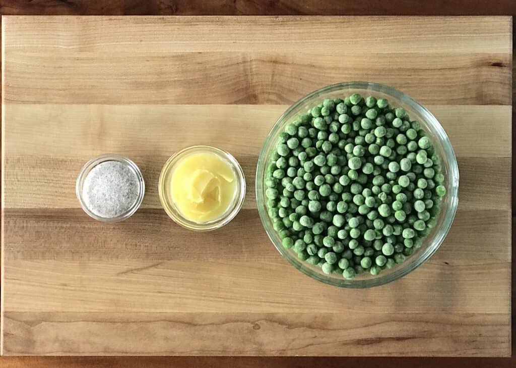 frozen green peas, butter and salt, all in glass bowls on a wooden cutting board