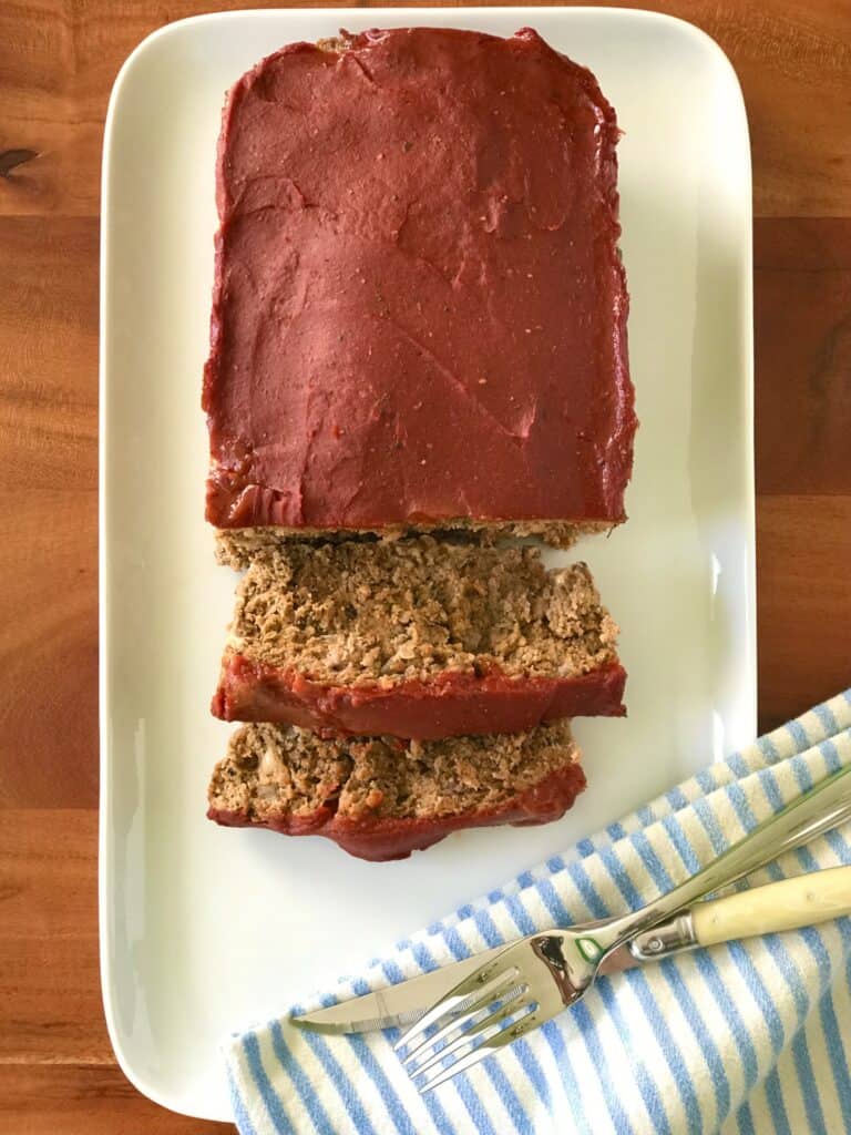 Whole30 meatloaf on a white platter with a blue striped towel, a knife and a fork.