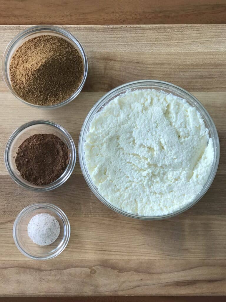 bowls of ricotta, coconut sugar, cocoa powder and salt on a wooden cutting board