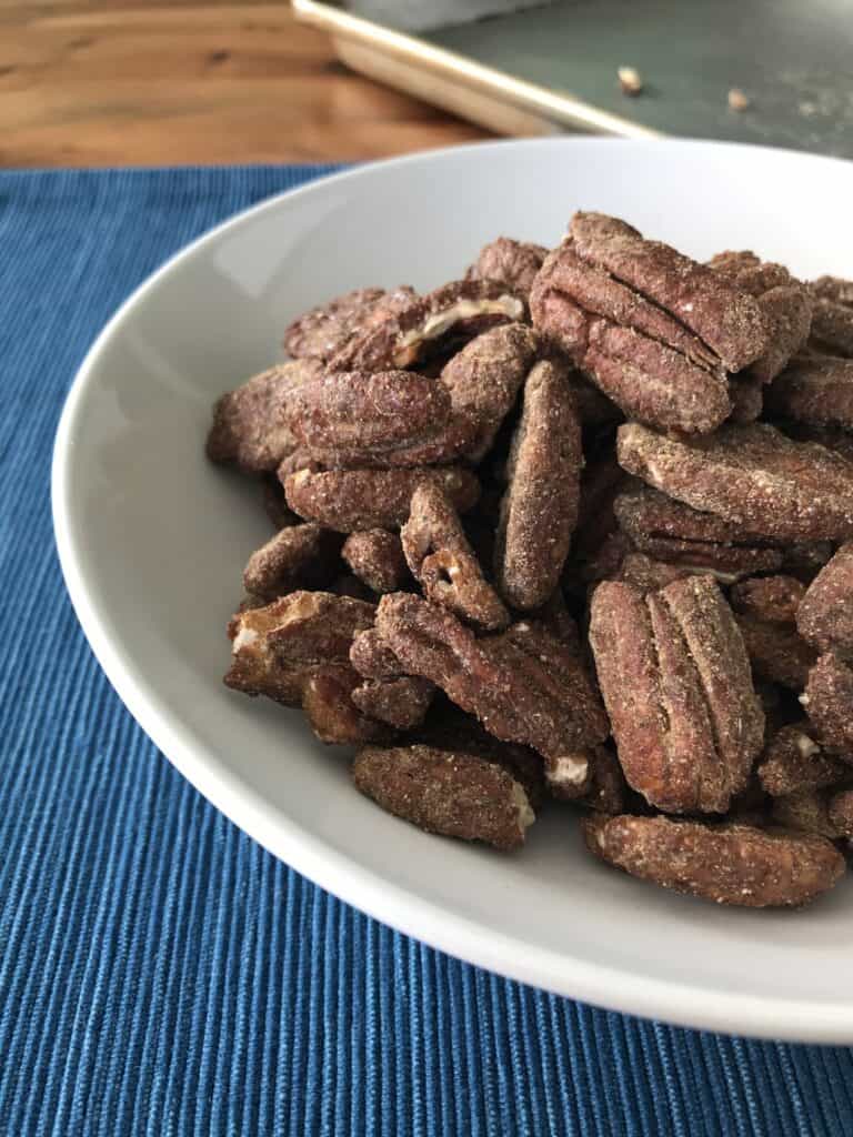 oven roasted pecans coated in spices in a white bowl on a blue table runner