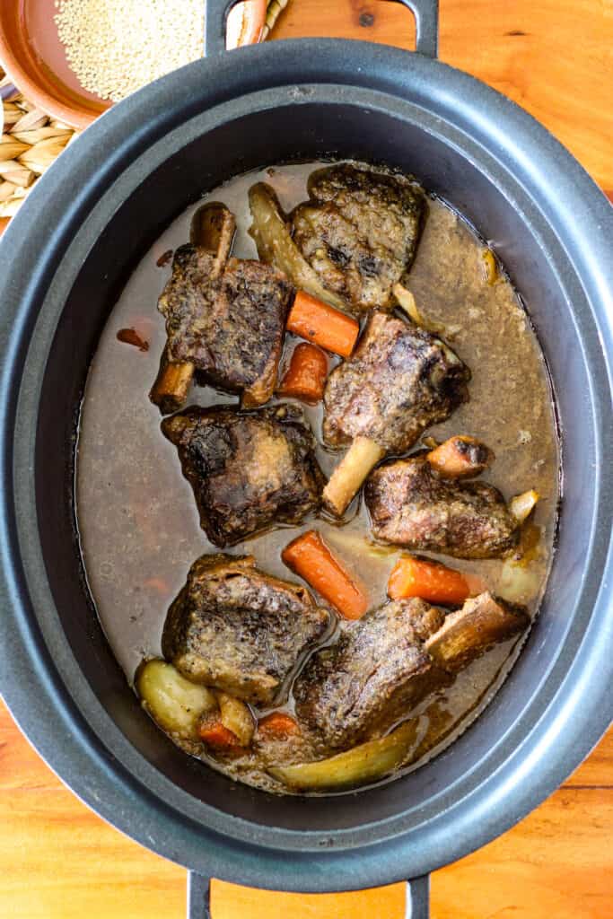 a crockpot insert full of short ribs and vegetables in a dark sauce