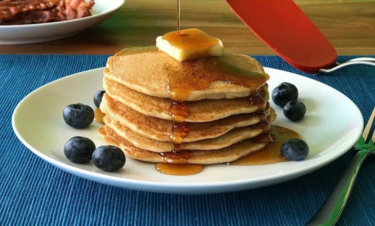 gluten-free pancakes made with coconut flour stacked on a plate with butter, maple syrup and blueberries on a white plate on a blue table runner