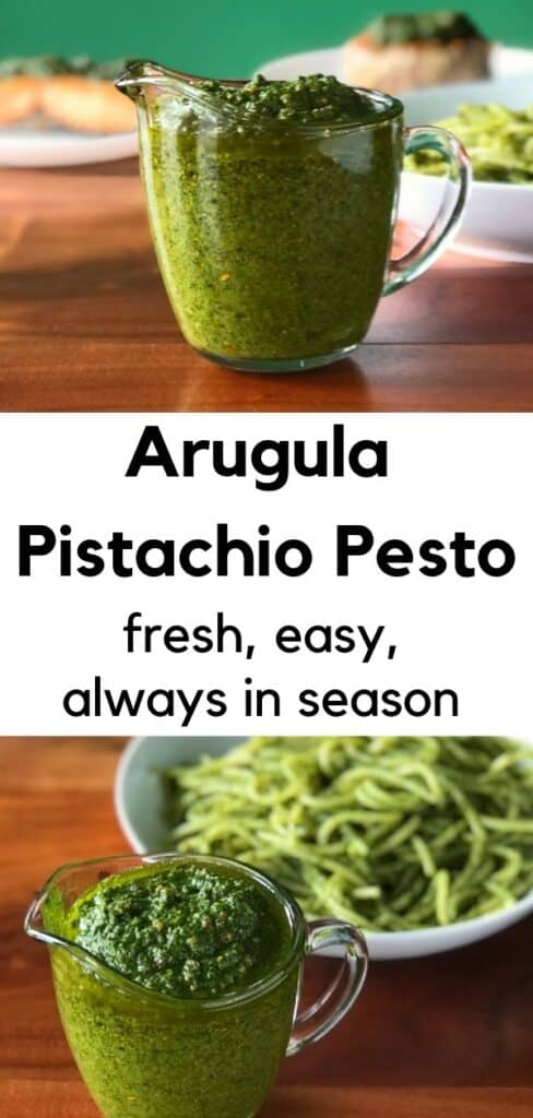 Arugula Pistachio Pesto in a small glass pitcher next to a bowl of spaghetti coated in the sauce, all sitting on a wooden table