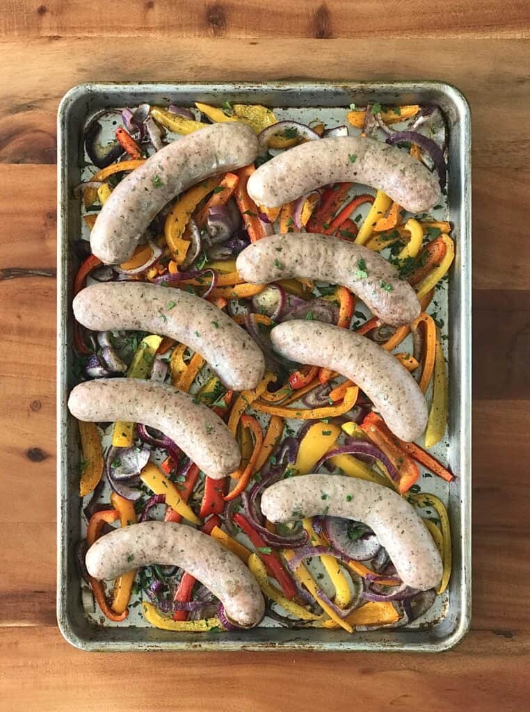 a baking sheet full of differently colored bell peppers, red onion slices and Italian sausages on top