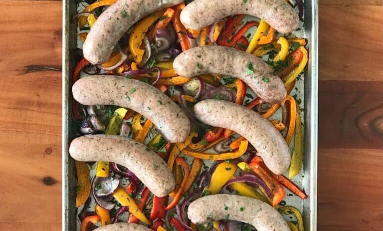 a baking sheet with sausages, peppers and onions