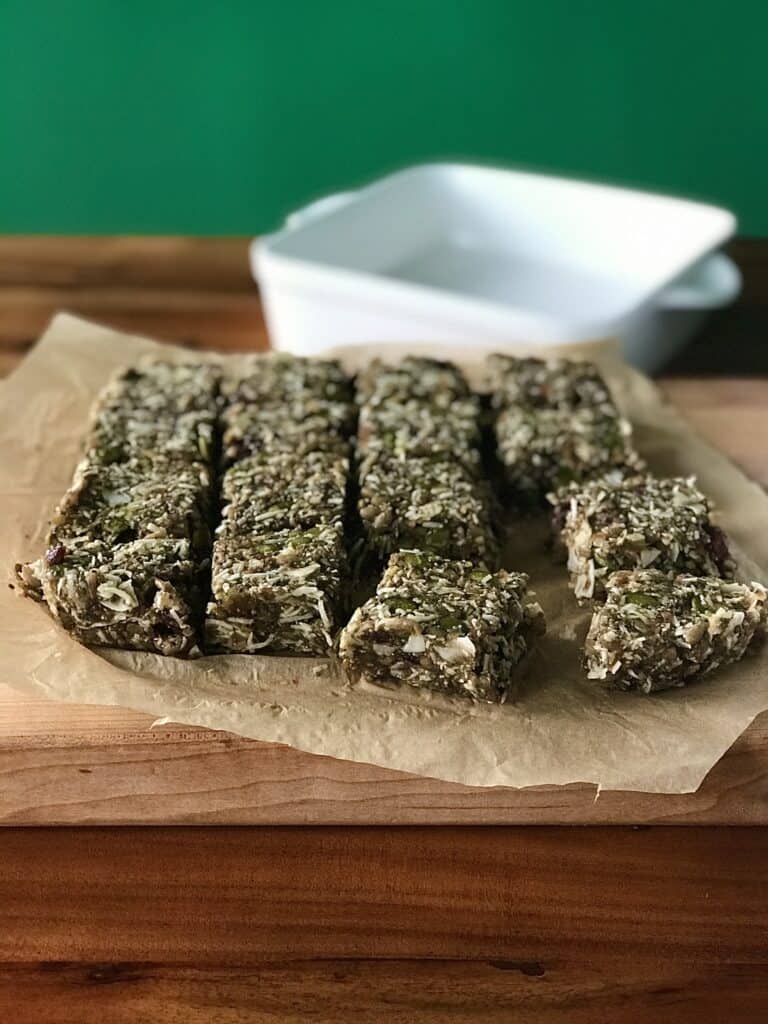 vegan breakfast bars on parchment paper on a wooden cutting board on a wooden table with a white baking dish in the background