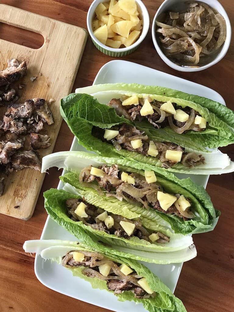 lettuce cups filled with Mexican pork, onions and pineapple on a white platter on a wooden table