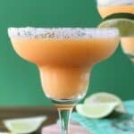 Frozen Peach Margaritas in margarita glasses with salted rims and lime wedges on the rims