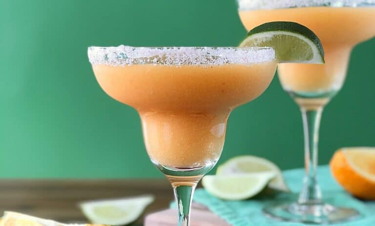 Frozen Peach Margaritas in margarita glasses with salted rims and lime wedges on the rims