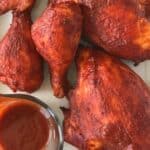 Chicken roasted in the oven with BBQ sauce on a white platter with a small glass pitcher of more sauce