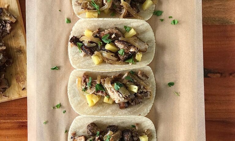 Mexican pork tacos lined up on parchment paper