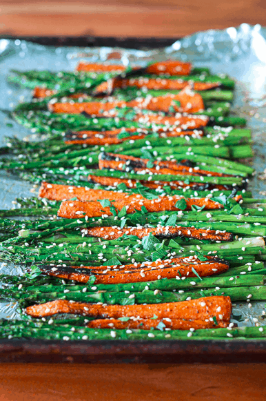 roasted vegetables lined up on a foil-lined baking sheet and sprinkled with sesame seeds and chopped parsley