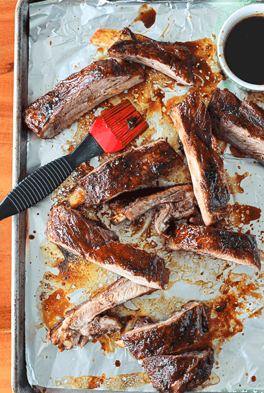 spare ribs coated in a sticky glaze on a foil-lined baking sheet with a silicone brush