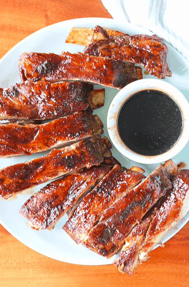 individual Chinese spare ribs on a white round plate with a small bowl of dark sauce