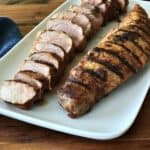 2 grilled pork tenderloins - one whole, one sliced - on a white platter on a wooden table