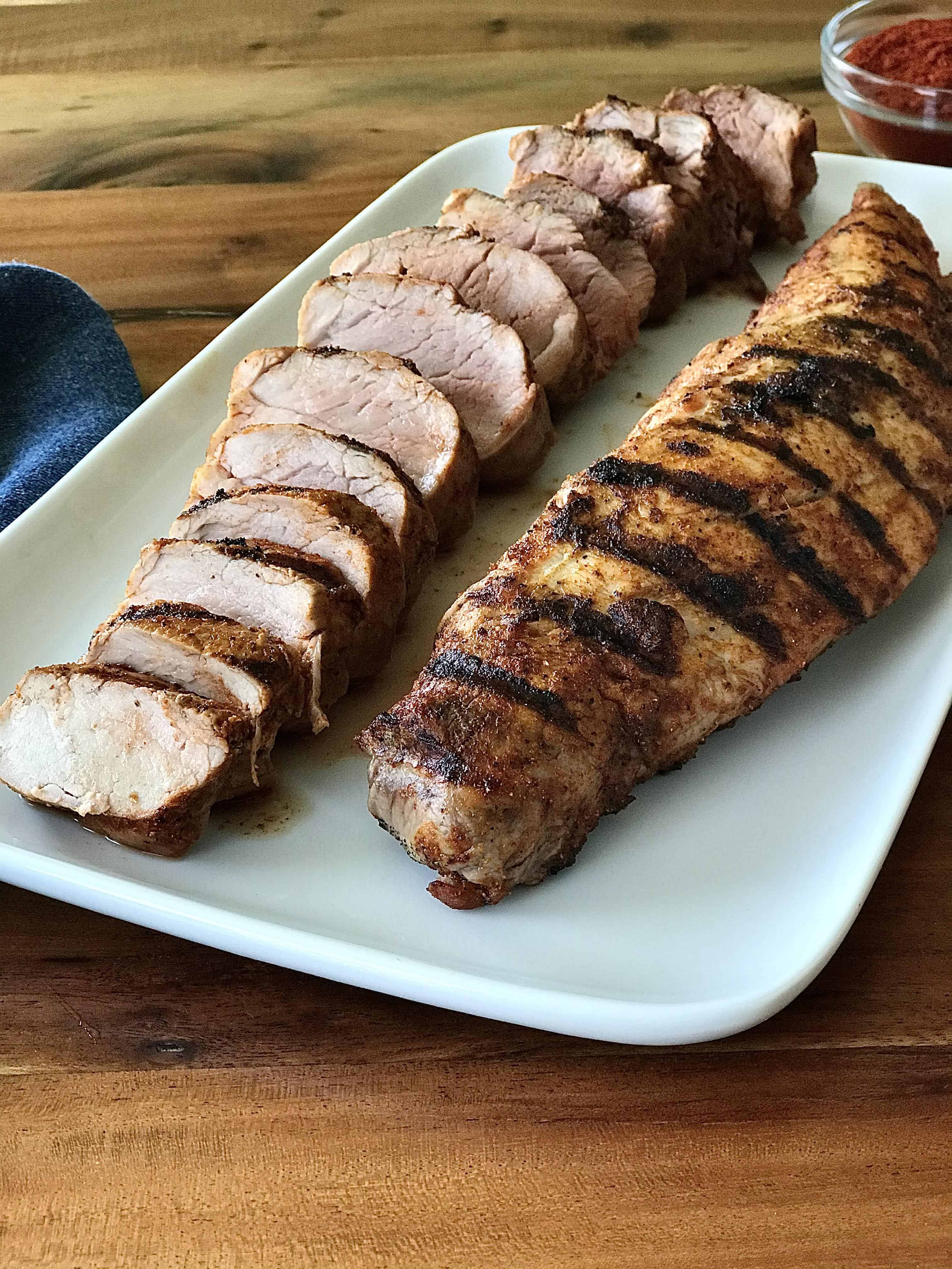 2 grilled pork tenderloins - one whole, one sliced - on a white platter on a wooden table