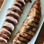 pork tenderloin that's been grilled and sliced on a white platter on a wooden table