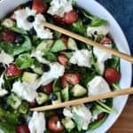 a spinach berry salad with burrata, sunflower seeds and cucumber on a wooden table