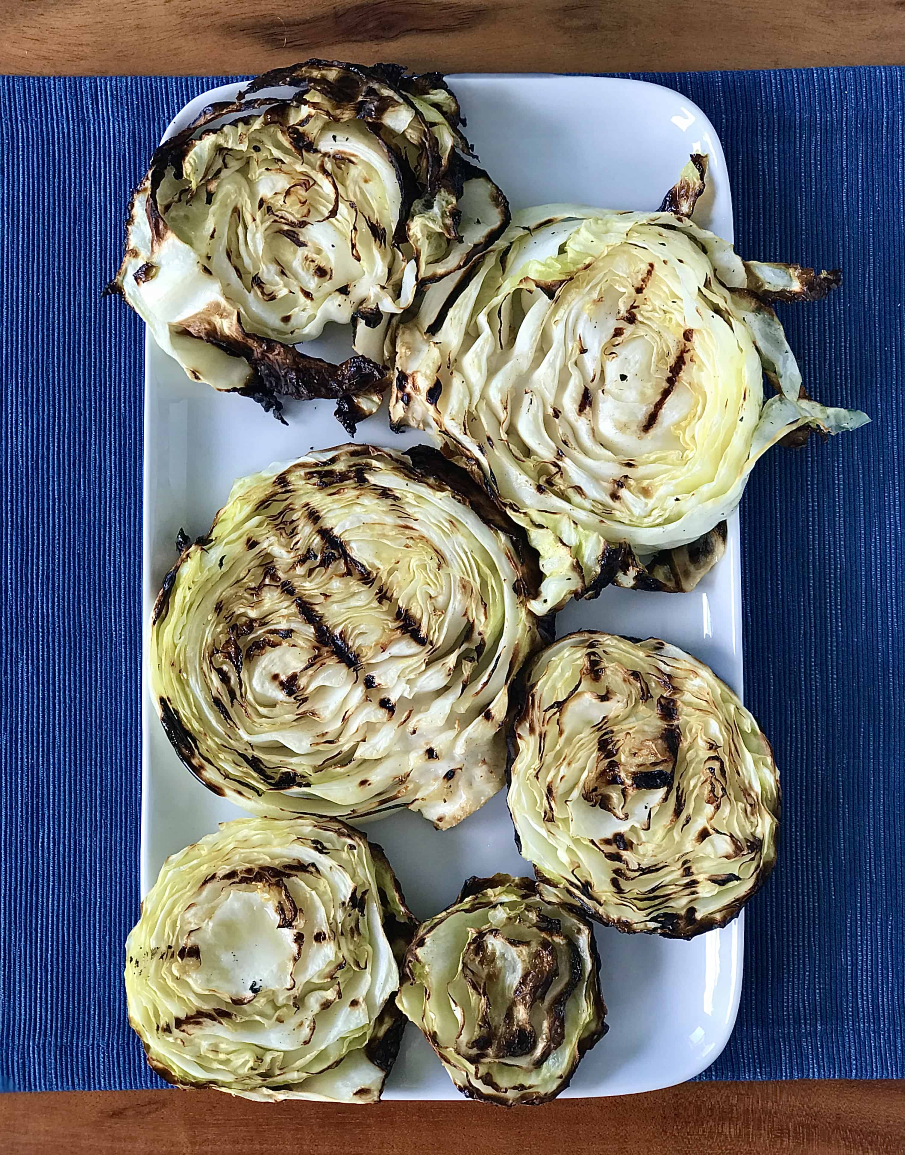 grilled cabbage steaks on a white platter on a blue table runner