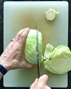 Two hands slicing a cabbage on a white cutting board