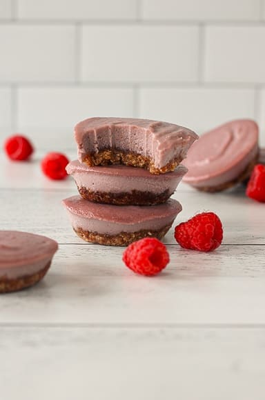 dairy-free raspberry cheesecake bites stacked on top of each other and the top one has a bite taken out of it