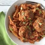 healthy turkey meatballs with parsnip noodles in a white bowl with a fork next to a green napkin