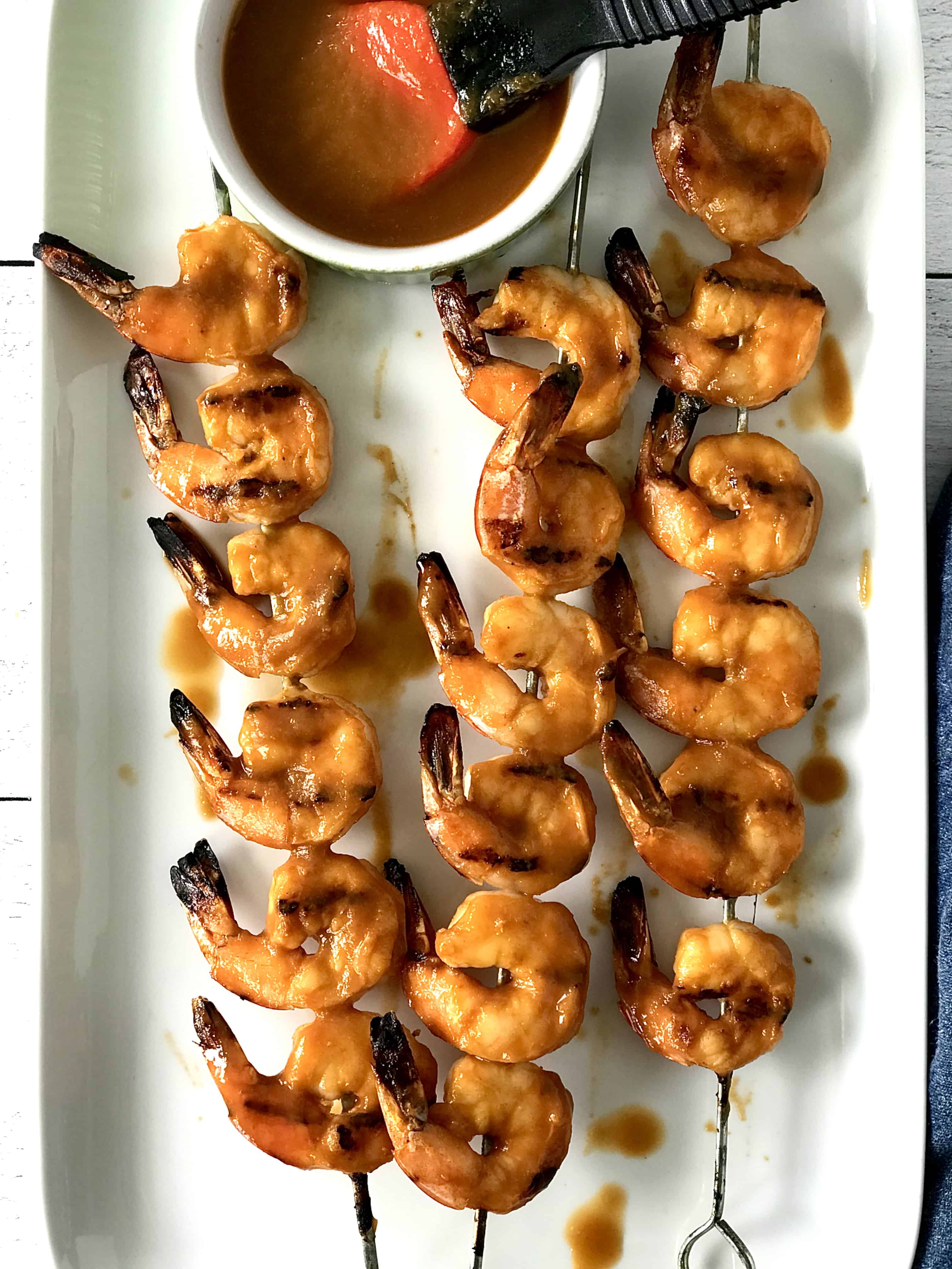 healthy grilled shrimp kebabs on a long white platter brushed with a tangy BBQ sauce