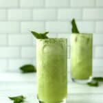a green mocktail in 2 tall glasses topped with mint sprigs