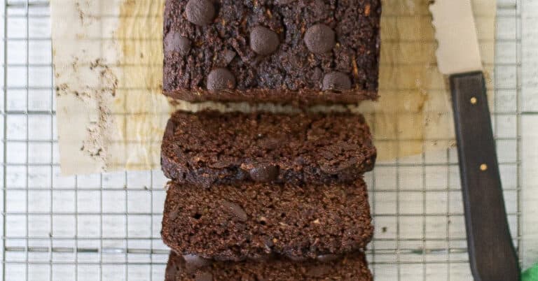 Healthy chocolate zucchini bread sliced on a cooling rack next to a serrated knife