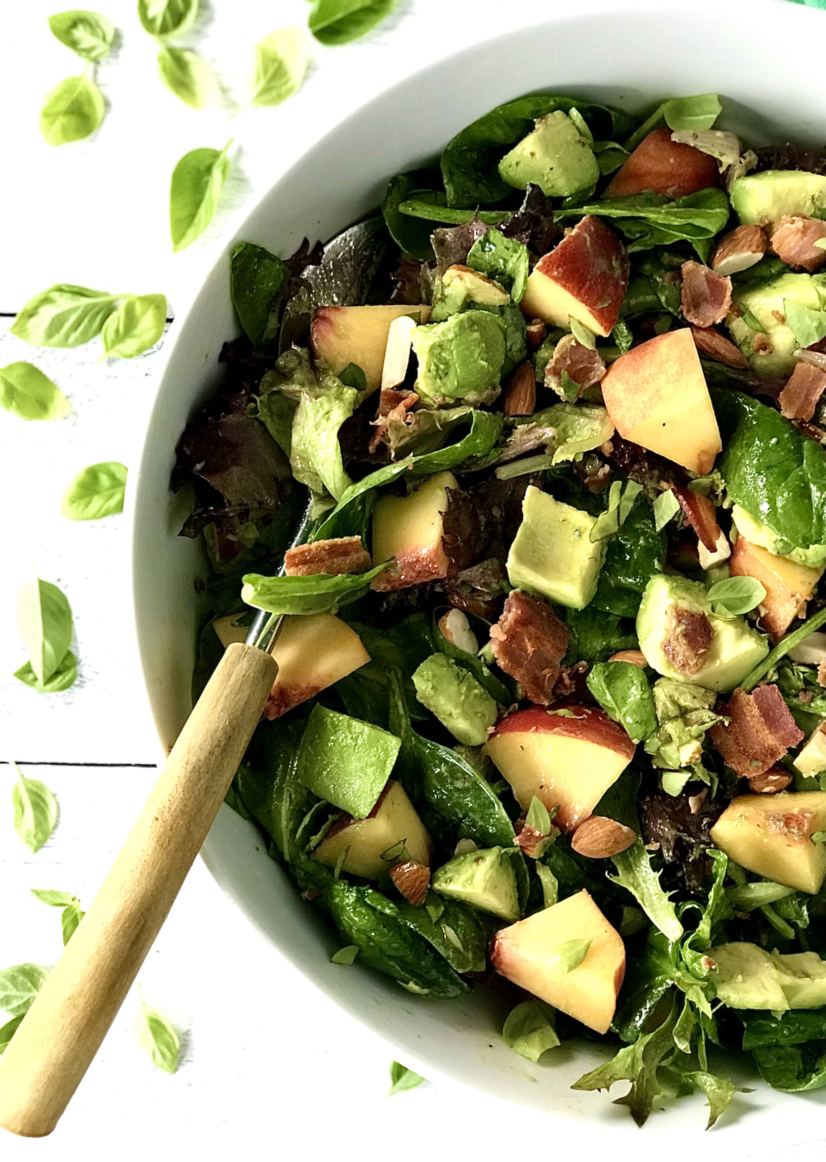 a big white bowl with a big salad with chunks of peach and avocado, plus almonds and bacon