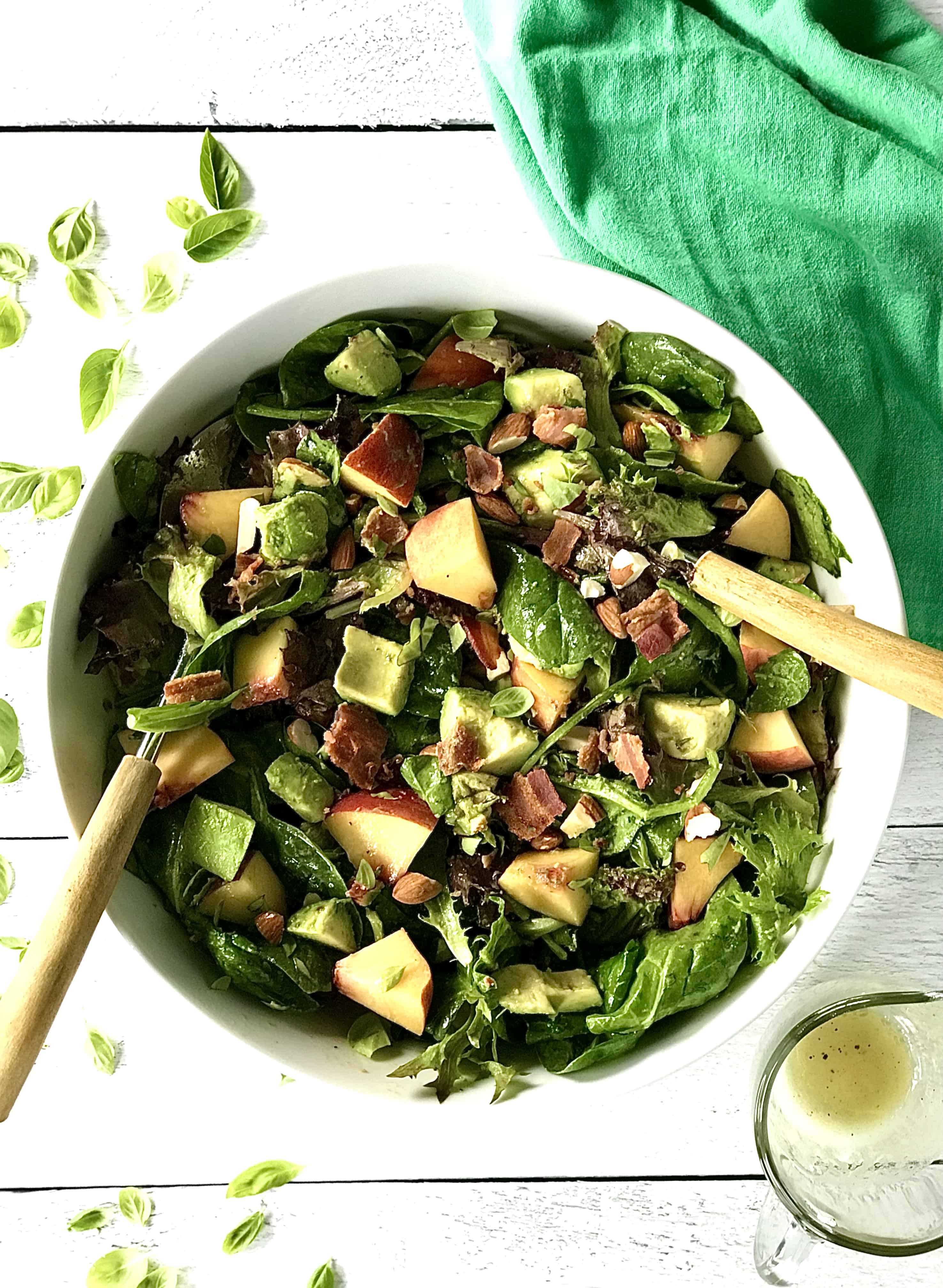 A fresh summer salad in a big white bowl full of peaches, avocado, almonds, bacon, basil and leafy greens