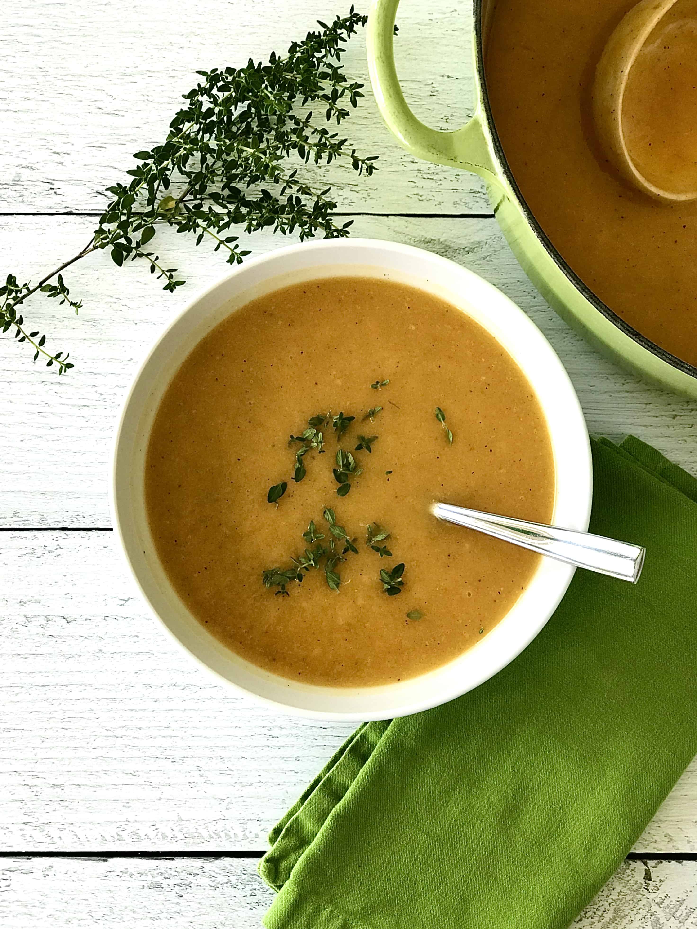 roasted apple and butternut soup in a white bowl with a spoon and garnished with fresh thyme