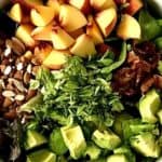 a white bowl full of peaches, avocado, chopped bacon, chopped almonds, chopped basil and leafy greens