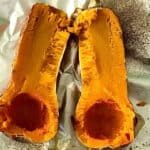 a roasted butternut squash split in half and seeded on a foil-lined baking sheet
