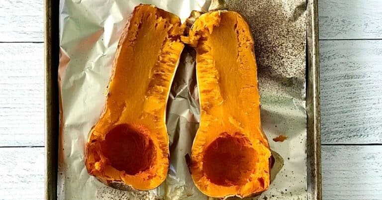 a roasted butternut squash split in half and seeded on a foil-lined baking sheet