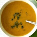 Butternut squash soup in a white bowl with a spoon and garnished with fresh thyme, sitting on a white wooden table