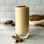 a protein smoothie made with sweet potato in a tall glass next to a cinnamon stick and half a nutmeg