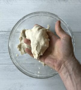 a hand holding up paleo pie crust over a glass bowl of more mix