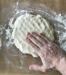 a hand patting out paleo pie dough on parchment paper over a pastry board