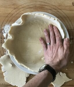 a hand patting paleo pie dough into a pie dish