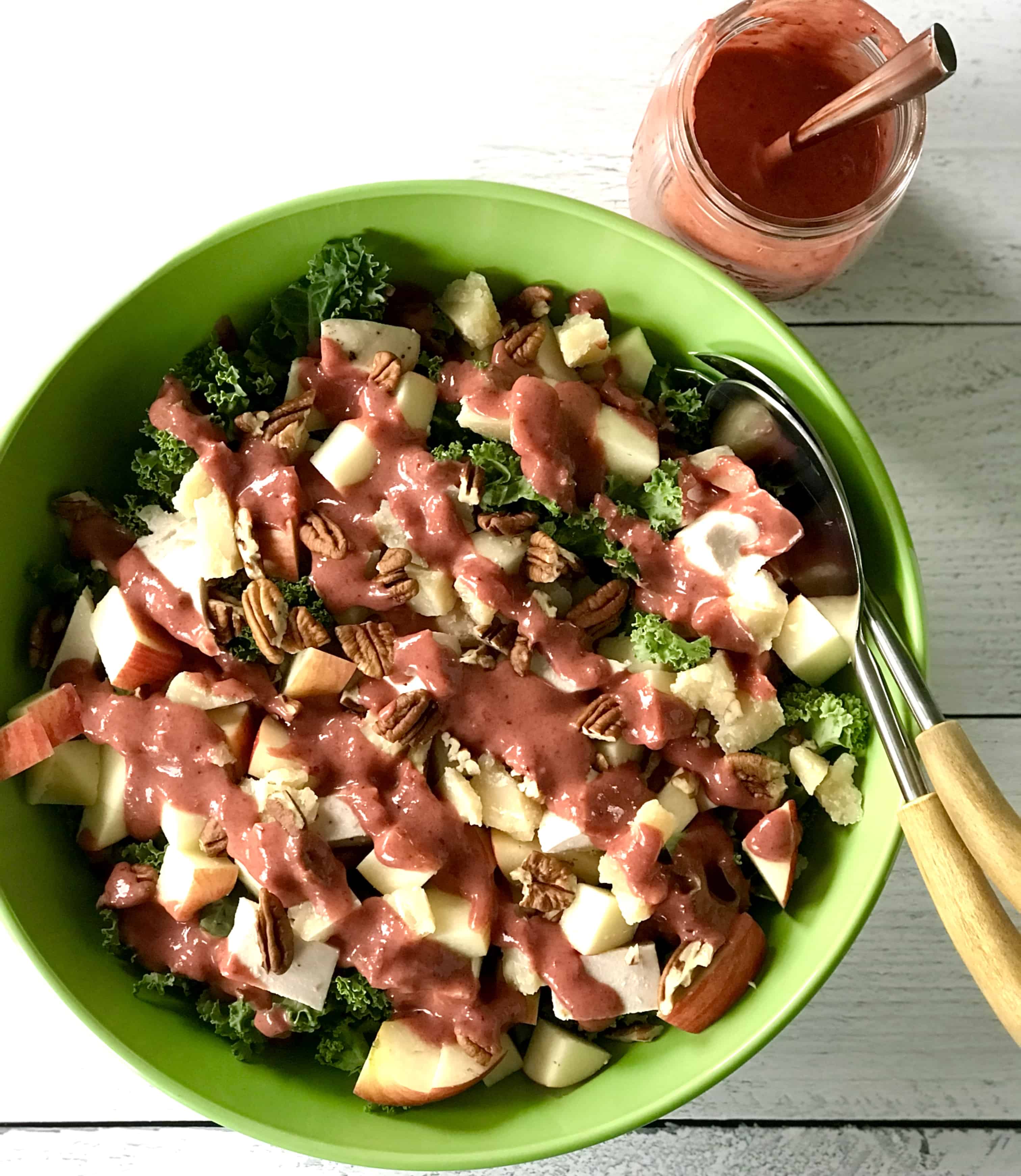 a salad in a bowl with kale, chicken, apples, pecans and Parmesan, topped with a cranberry dressing