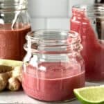 cranberry salad dressings in mason jars surrounded by ginger, lime wedges and bottles of condiments