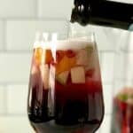 a wine glass is full of sangria and fruit and bottle of bubbly wine is poured on top