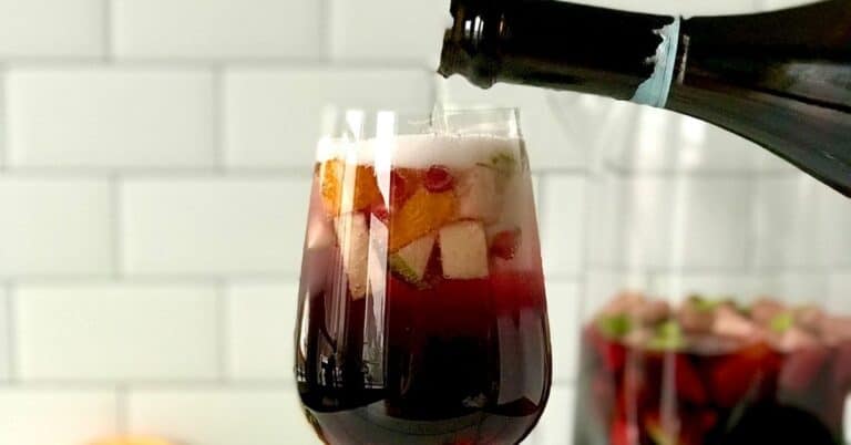 a wine glass is full of sangria and fruit and bottle of bubbly wine is poured on top